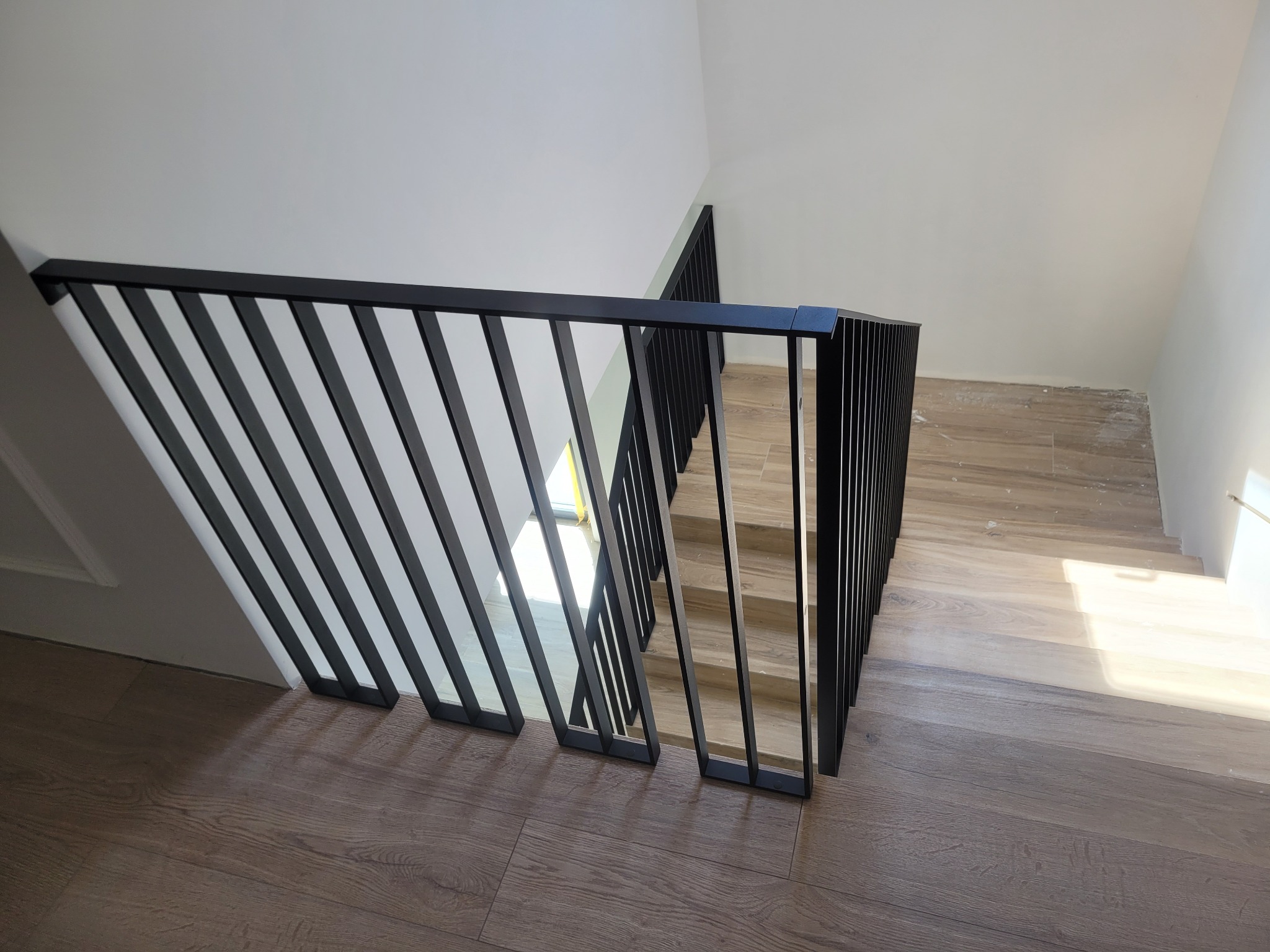 Nowoczesne schody z drewnianymi stopniami i czarną, minimalistyczną balustradą z pionowych prętów, widok z góry.