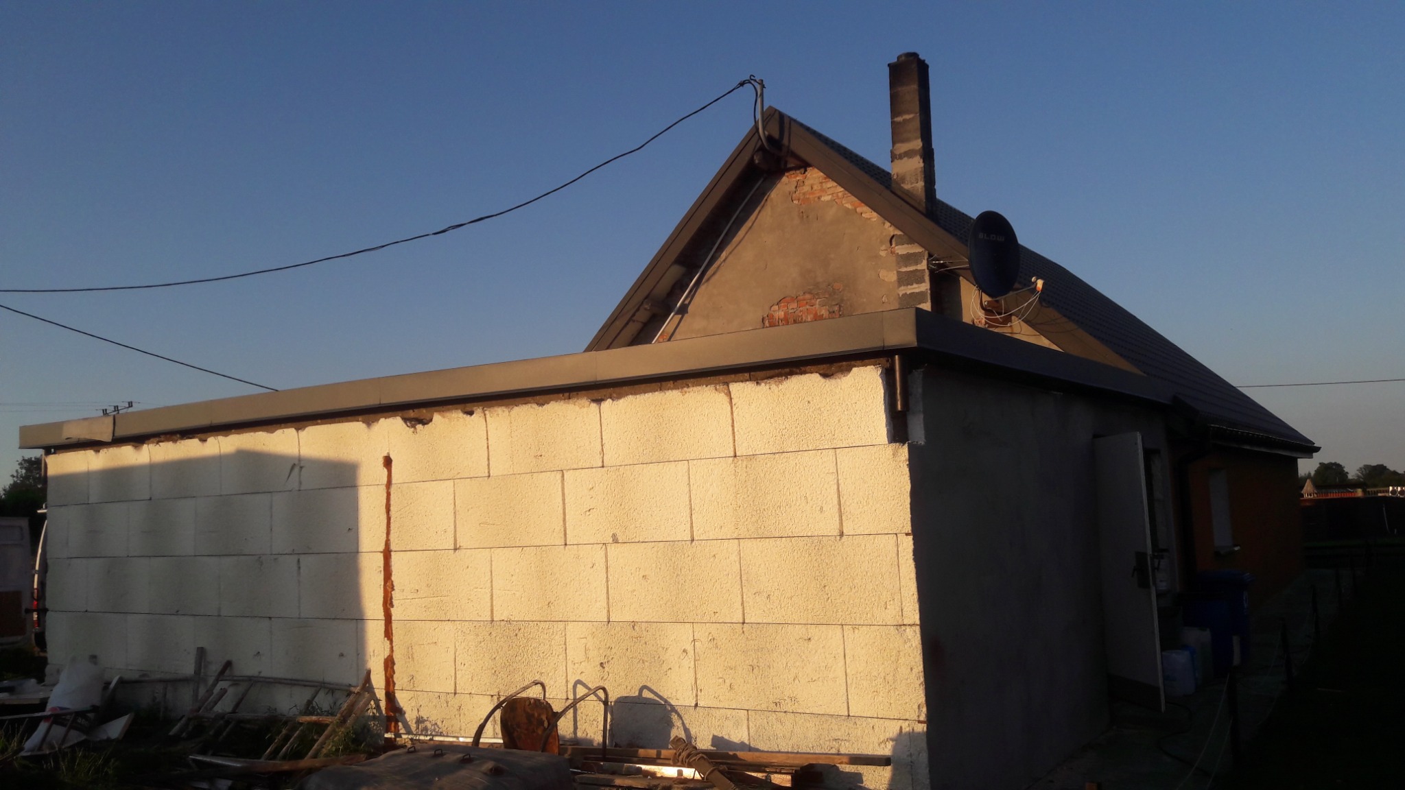 Budynek z białego bloczka z nowym dachem i orynnowaniem, widoczny komin z satelitą, w tle błękitne niebo.