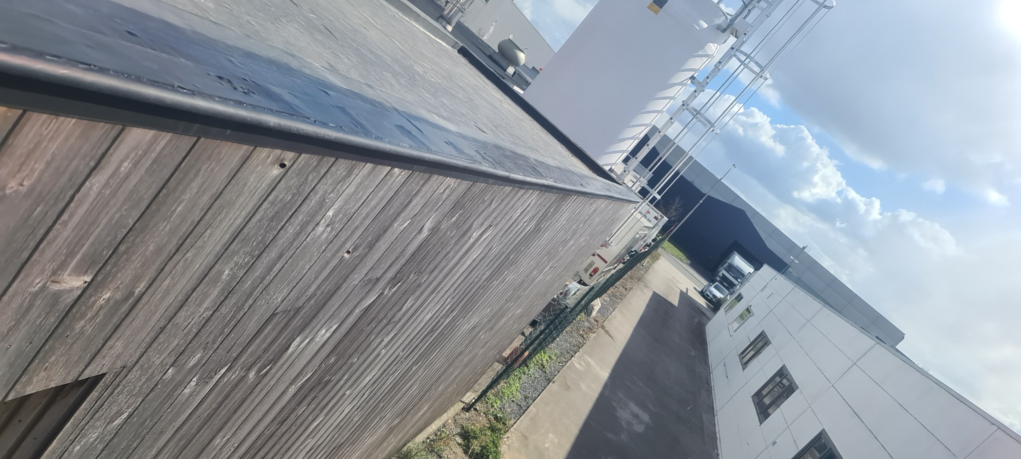 Płaski dach budynku przemysłowego z deskowaną attyką, widok z góry na tle błękitnego nieba z chmurami.