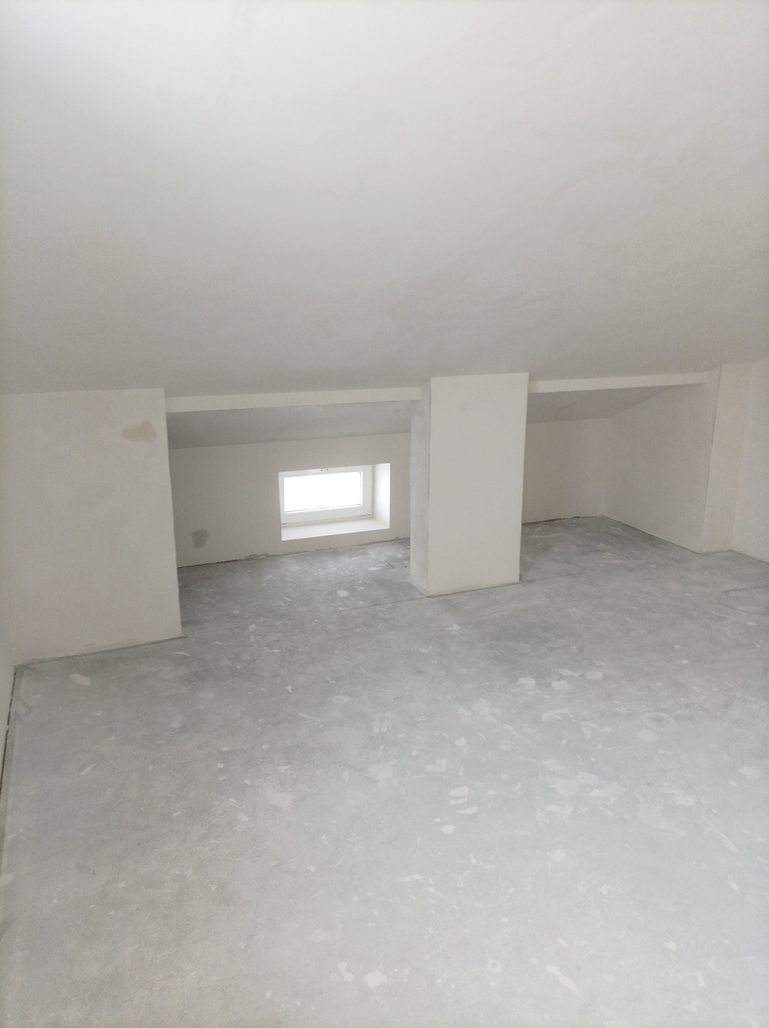 Wnętrze poddasza po wykonaniu gładzi gipsowych na ścianach i suficie, widoczne nierówności na podłodze.