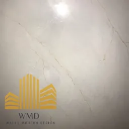 Fragment ściany wykończonej jasnym, marmurkowym materiałem z delikatnymi złotymi żyłkami, w rogu widoczne logo firmy 'WMD Walls Modern Design'.