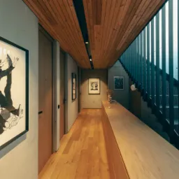 Wnętrze korytarza z drewnianą podłogą, sufitem i zabudową, betonowymi ścianami, obrazami w ramach i schodami z metalową balustradą.