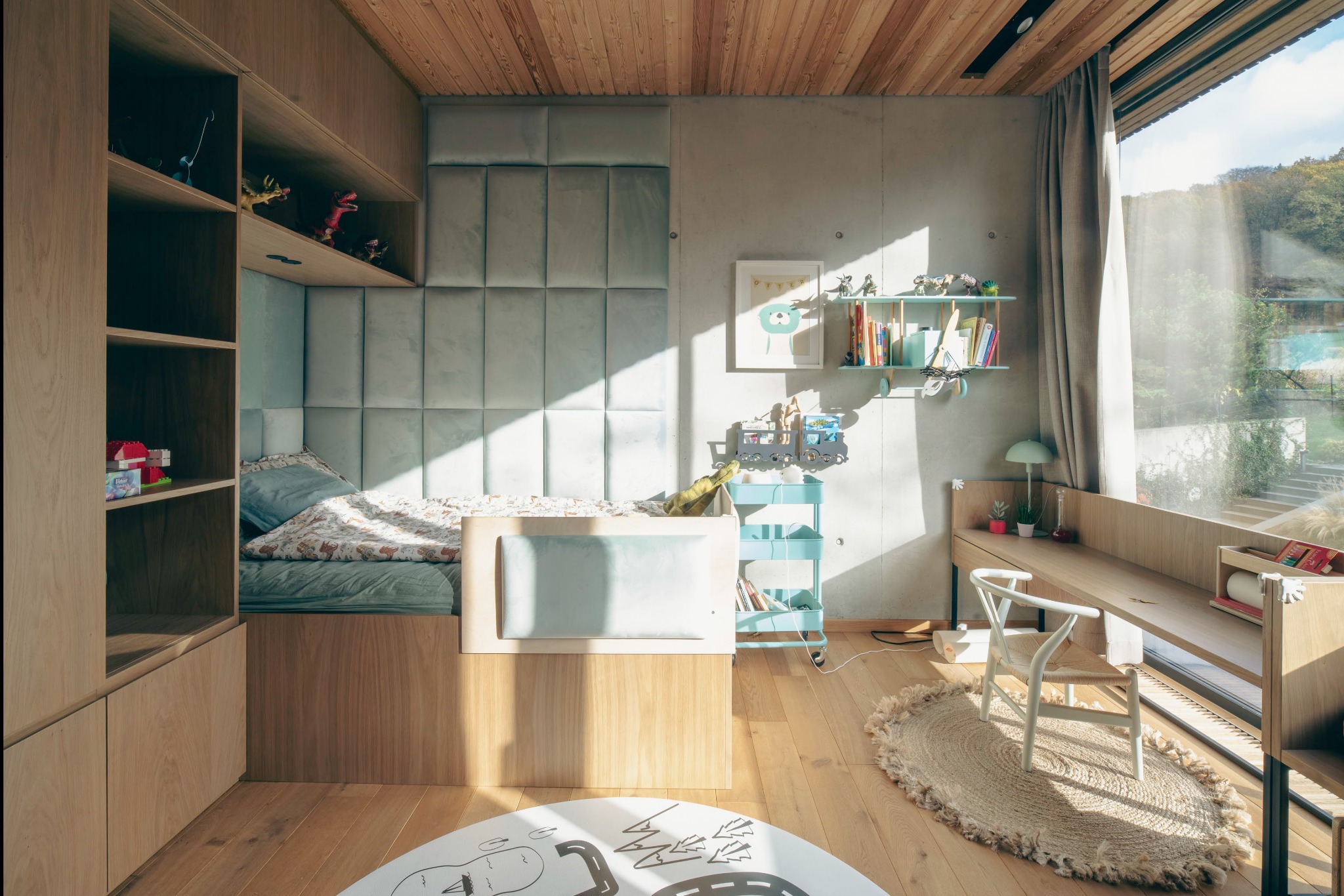 Jasne, minimalistyczne wnętrze pokoju dziecięcego z drewnianą zabudową, łóżkiem z tapicerowanym zagłówkiem i biurkiem przy oknie, oświetlone naturalnym światłem