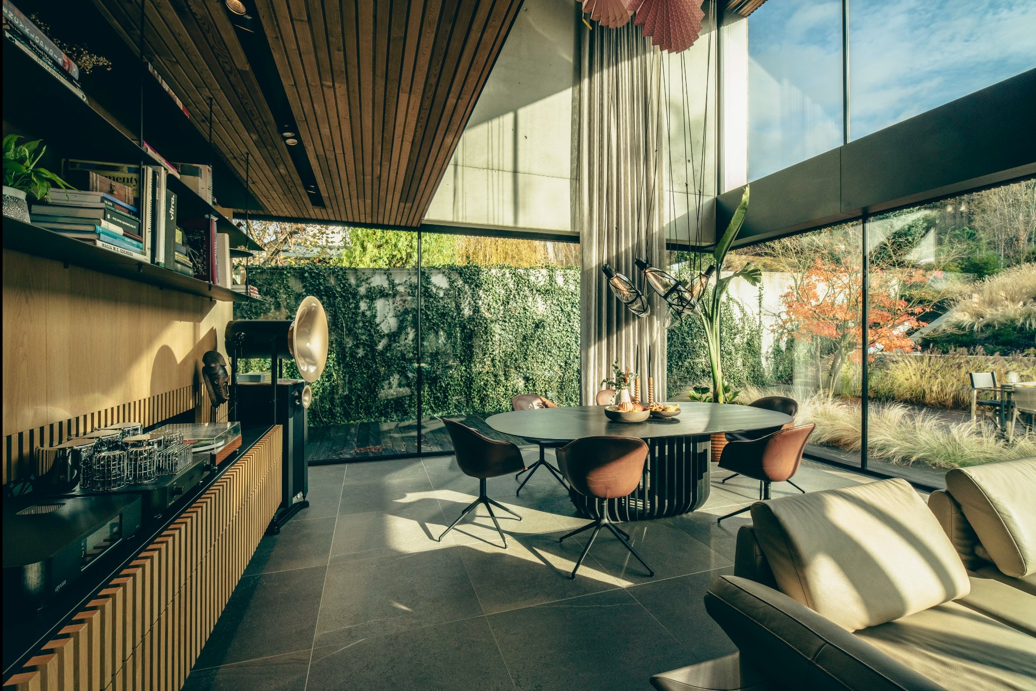 Nowoczesny salon z panoramicznymi oknami, okrągłym stołem i gramofonem z tubą, z widokiem na zielony ogród.