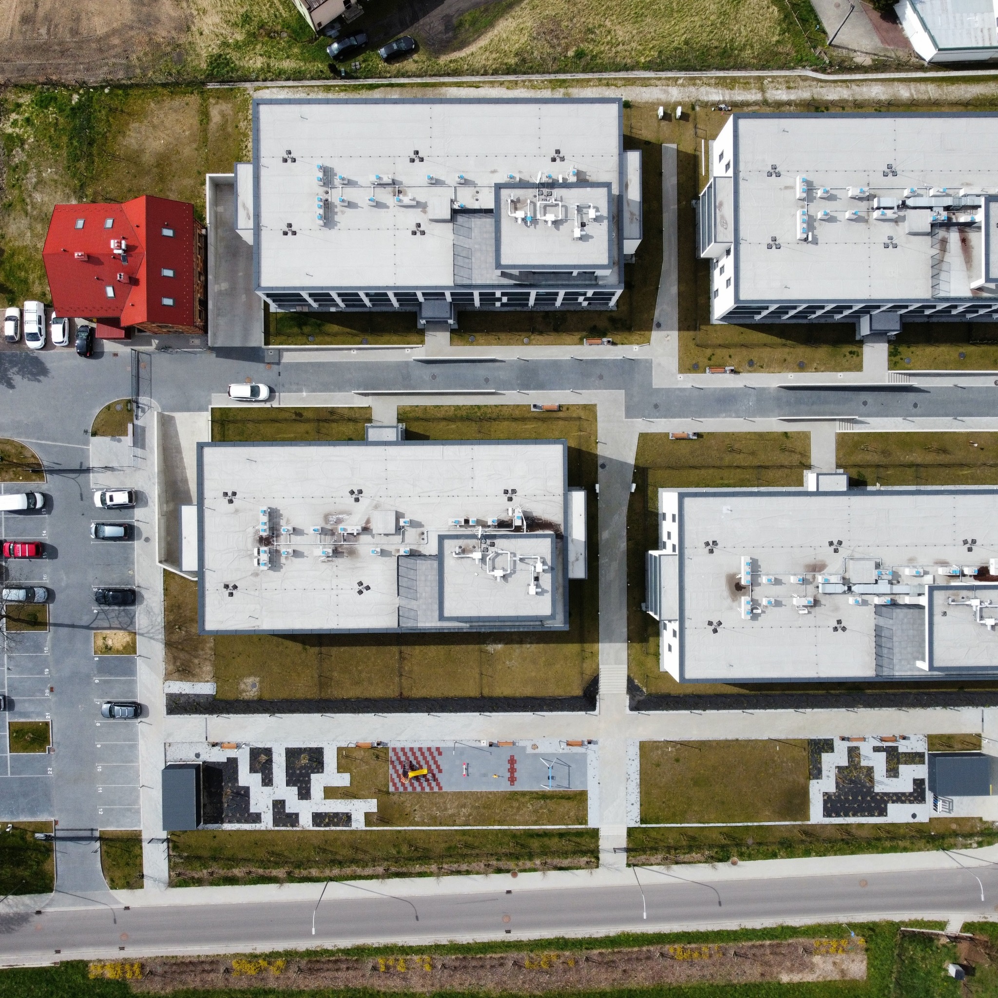 Widok z lotu ptaka na kompleks nowoczesnych budynków biurowych z parkingiem i placem zabaw, otoczonych zielenią.