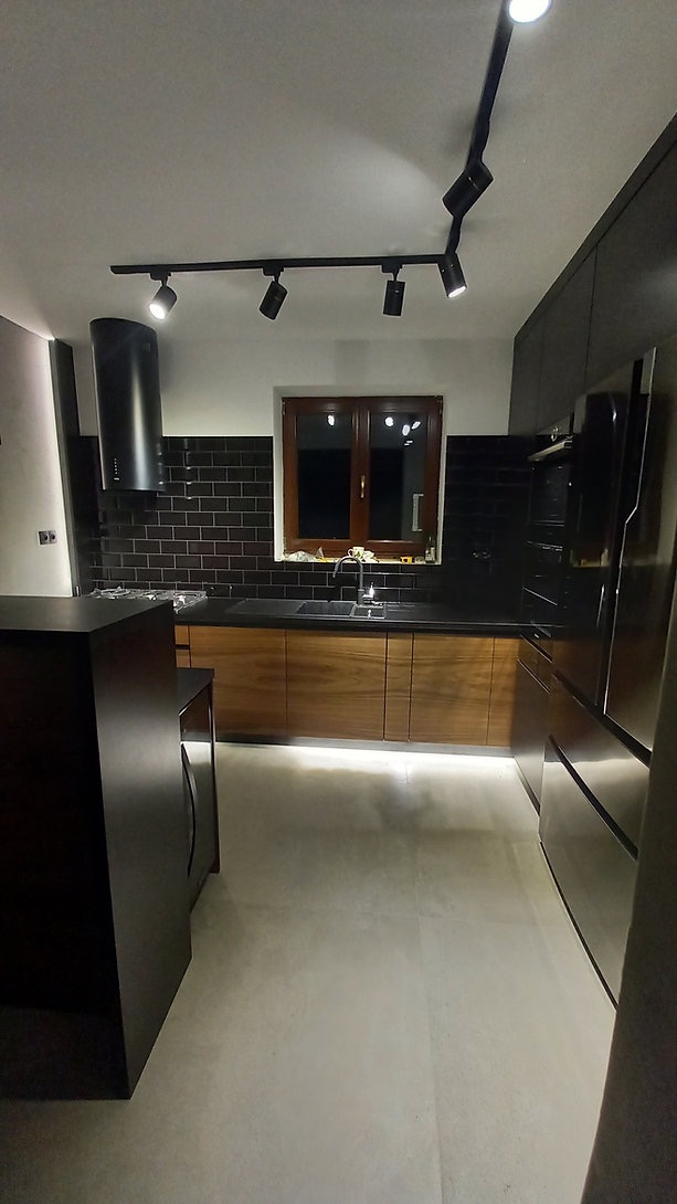 Nowoczesna kuchnia z drewnianymi frontami szafek, czarnymi płytkami na ścianie i oświetleniem punktowym na szynoprzewodzie.