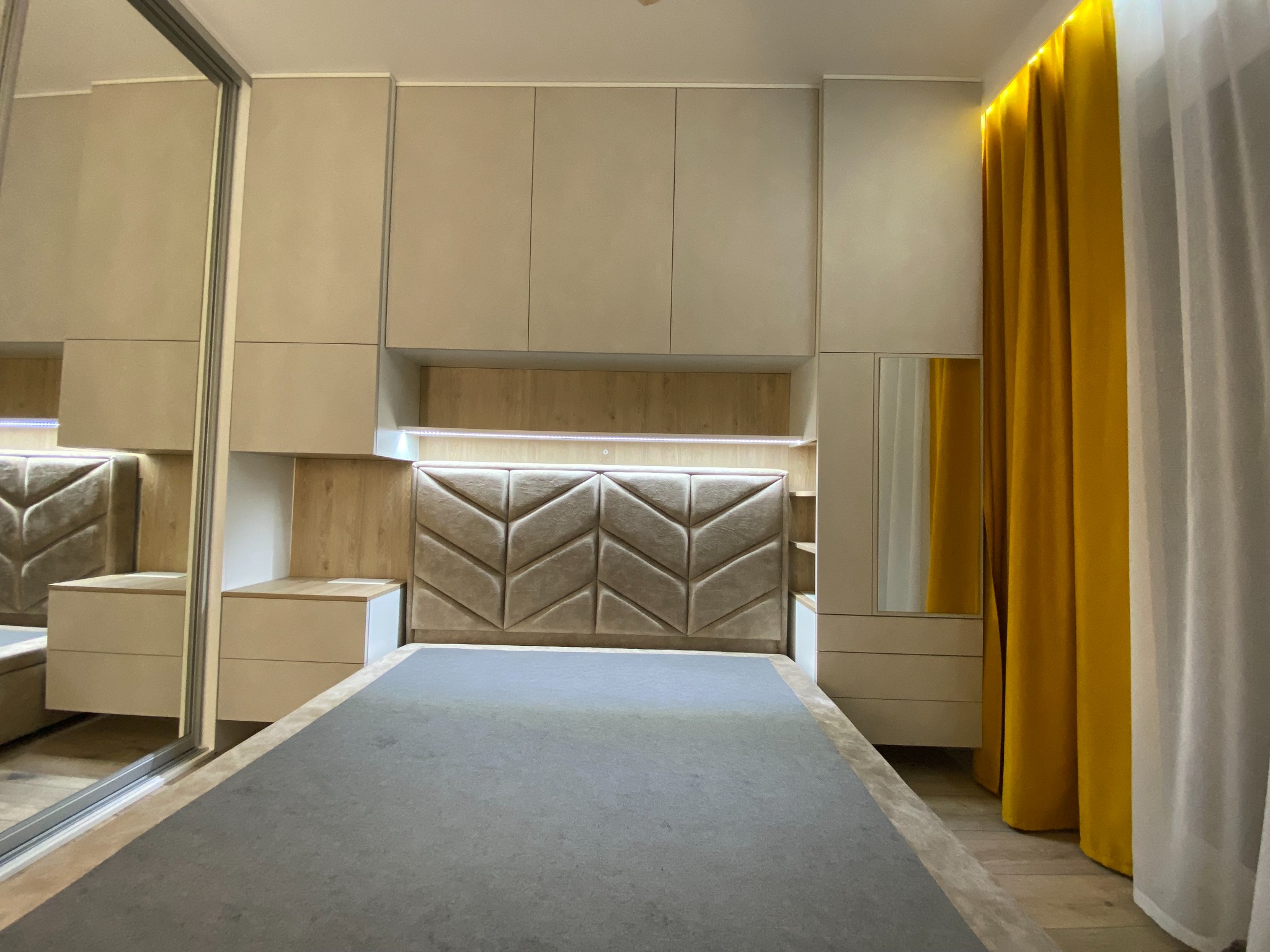 Kompletne wyposażenie sypialni w zabudowie: szafa z lustrem, szafki nocne i zagłówek z geometrycznym wzorem, oświetlenie LED i żółte zasłony.