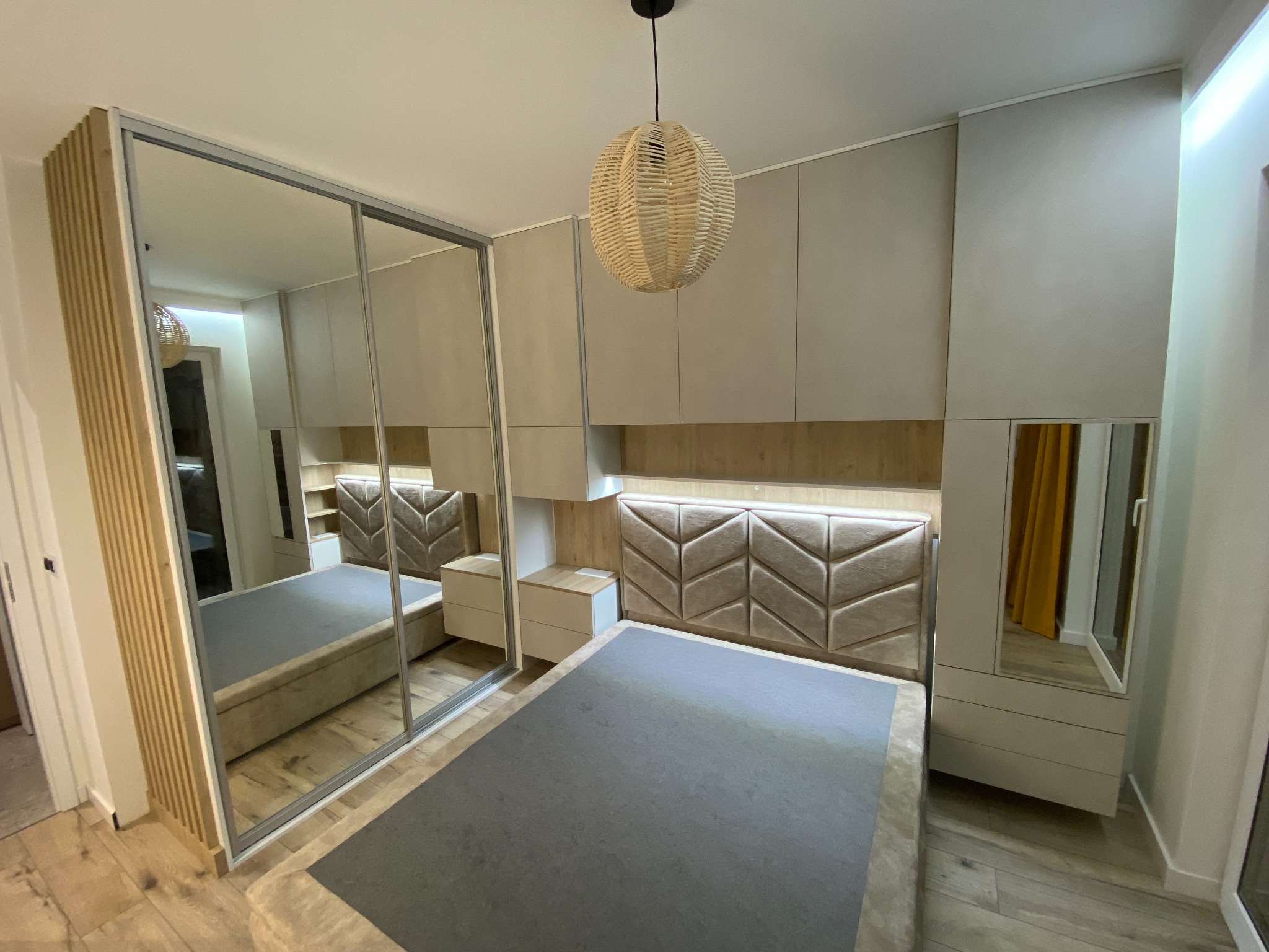 Sypialnia z beżowymi meblami na wymiar: szafa przesuwna z lustrem, łóżko z tapicerowanym zagłówkiem w geometryczny wzór, szafki nocne i wiszące szafki podświetlane LED.