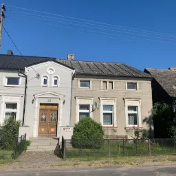 Dwa sąsiadujące, dwukondygnacyjne domy z cegły z numerem 23 nad drzwiami wejściowymi, oddzielone niewielkim, metalowym ogrodzeniem od ulicy.