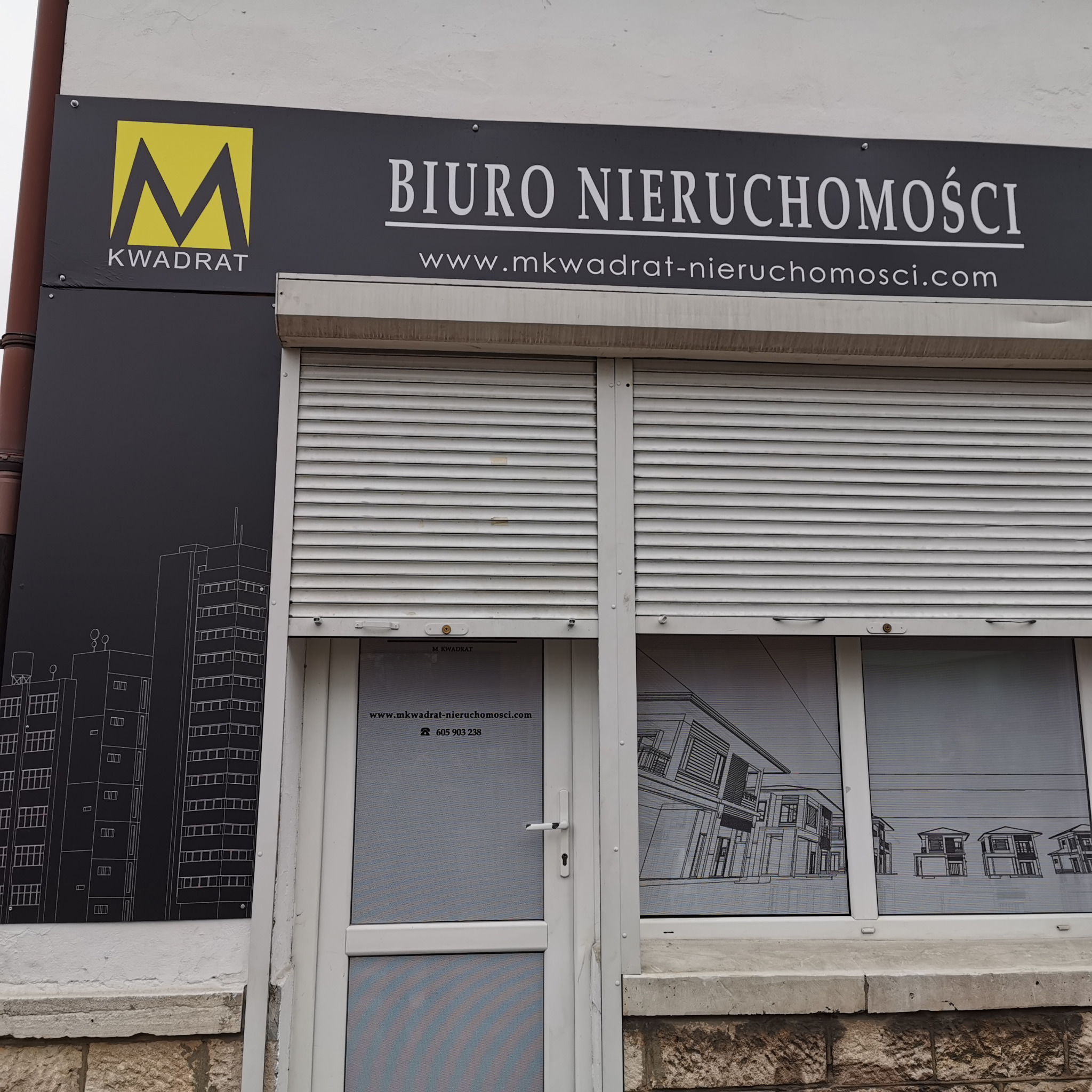 Fasada biura nieruchomości z logo firmy 'M Kwadrat', adresem strony internetowej i numerem telefonu, z częściowo zasłoniętymi roletami i grafikami budynków w oknach.