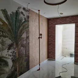 Pokój po częściowym położeniu tapet: jedna ściana z motywem dżungli, druga imitująca cegłę, widoczny laser krzyżowy i wiadro w sąsiednim pomieszczeniu.