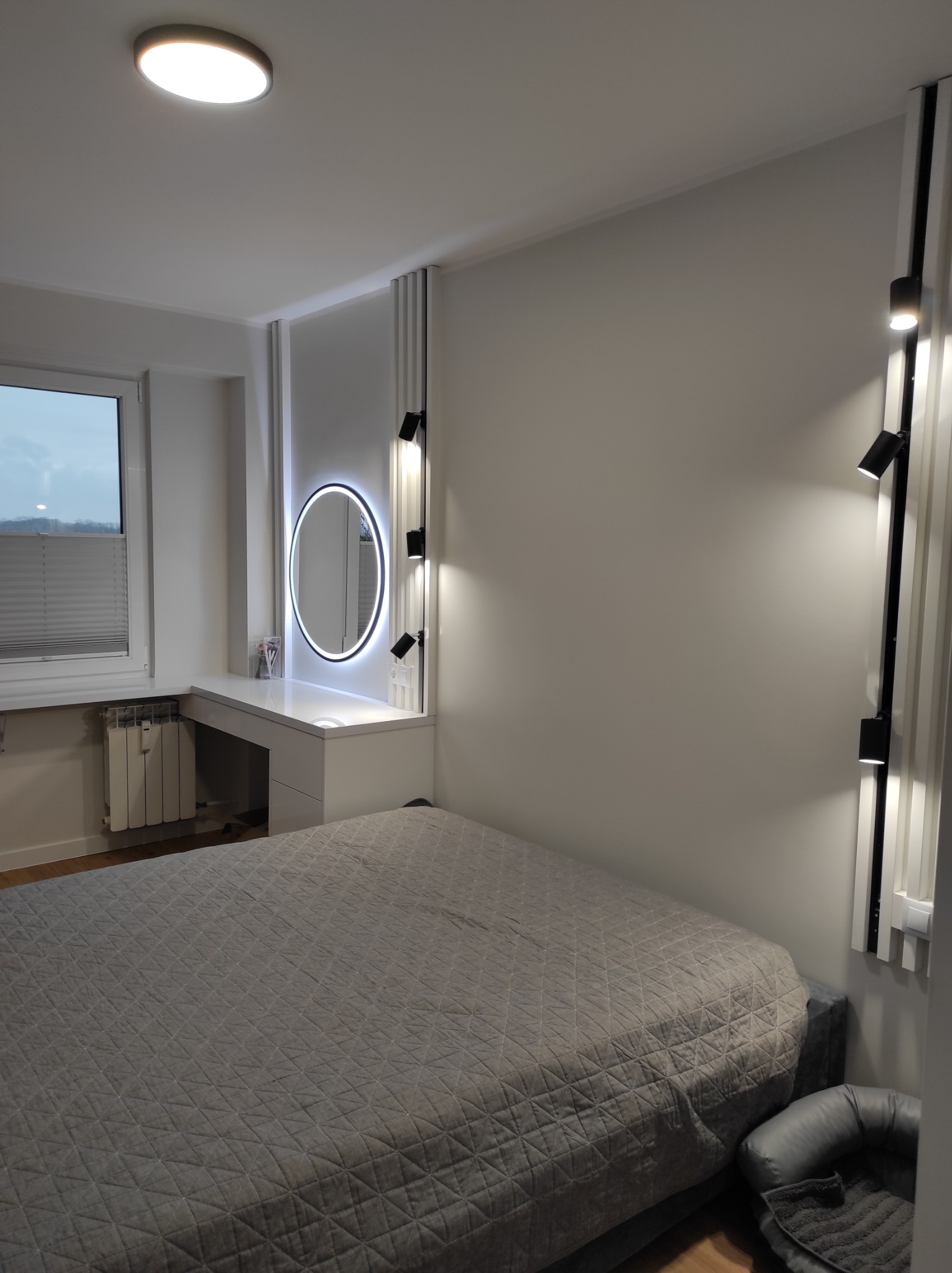 Nowoczesna sypialnia z łóżkiem, toaletką z podświetlanym lustrem i dekoracyjnymi panelami ściennymi z oświetleniem punktowym.