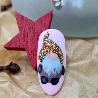 Paznokieć w kształcie migdała z jasnoróżowym tłem, ozdobiony ręcznie malowanym wzorem gnoma w brokatowej czapce, obok czerwona drewniana gwiazda i goździki.