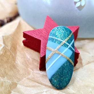 Pojedynczy, owalny tips z abstrakcyjną stylizacją: turkusowy brokat, jasnoniebieski mat i złote paski na tle papieru kraft i czerwonej gwiazdki.