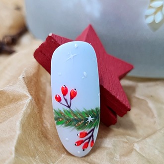Paznokieć z zimowym zdobieniem: gałązka świerku z czerwonymi owocami na jasnoniebieskim tle, obok czerwona, drewniana gwiazda.