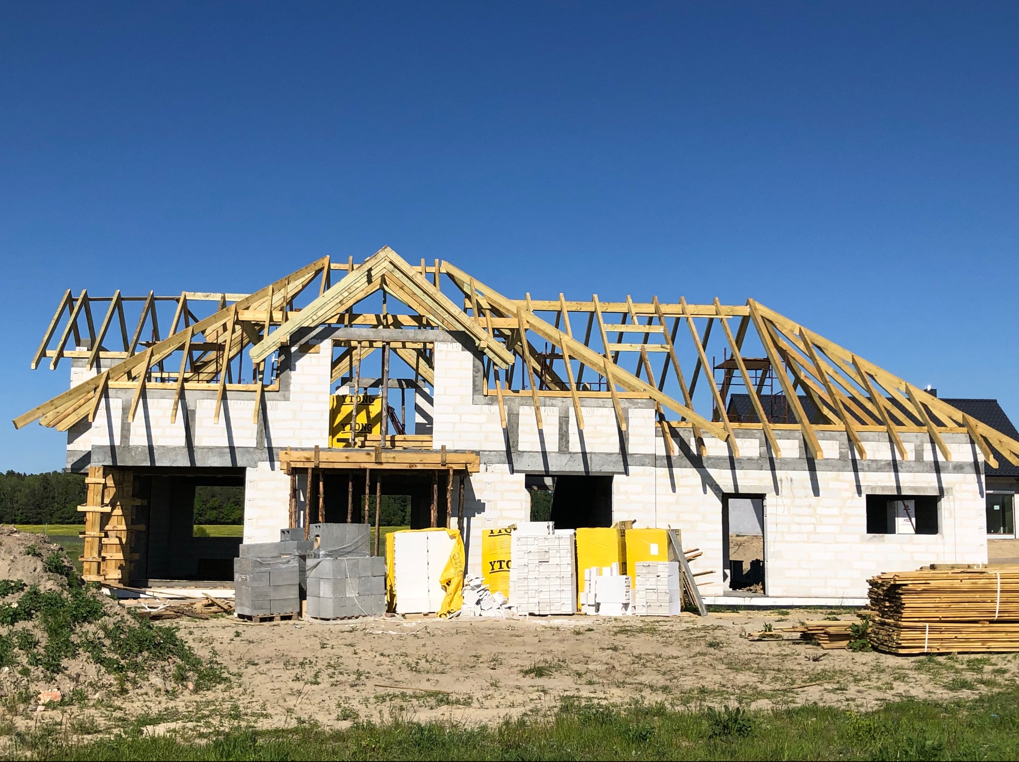 Budowa domu szkieletowego w trakcie: widoczne ściany z bloczków, drewniana konstrukcja dachu, materiały budowlane Ytong na placu budowy w słoneczny dzień.