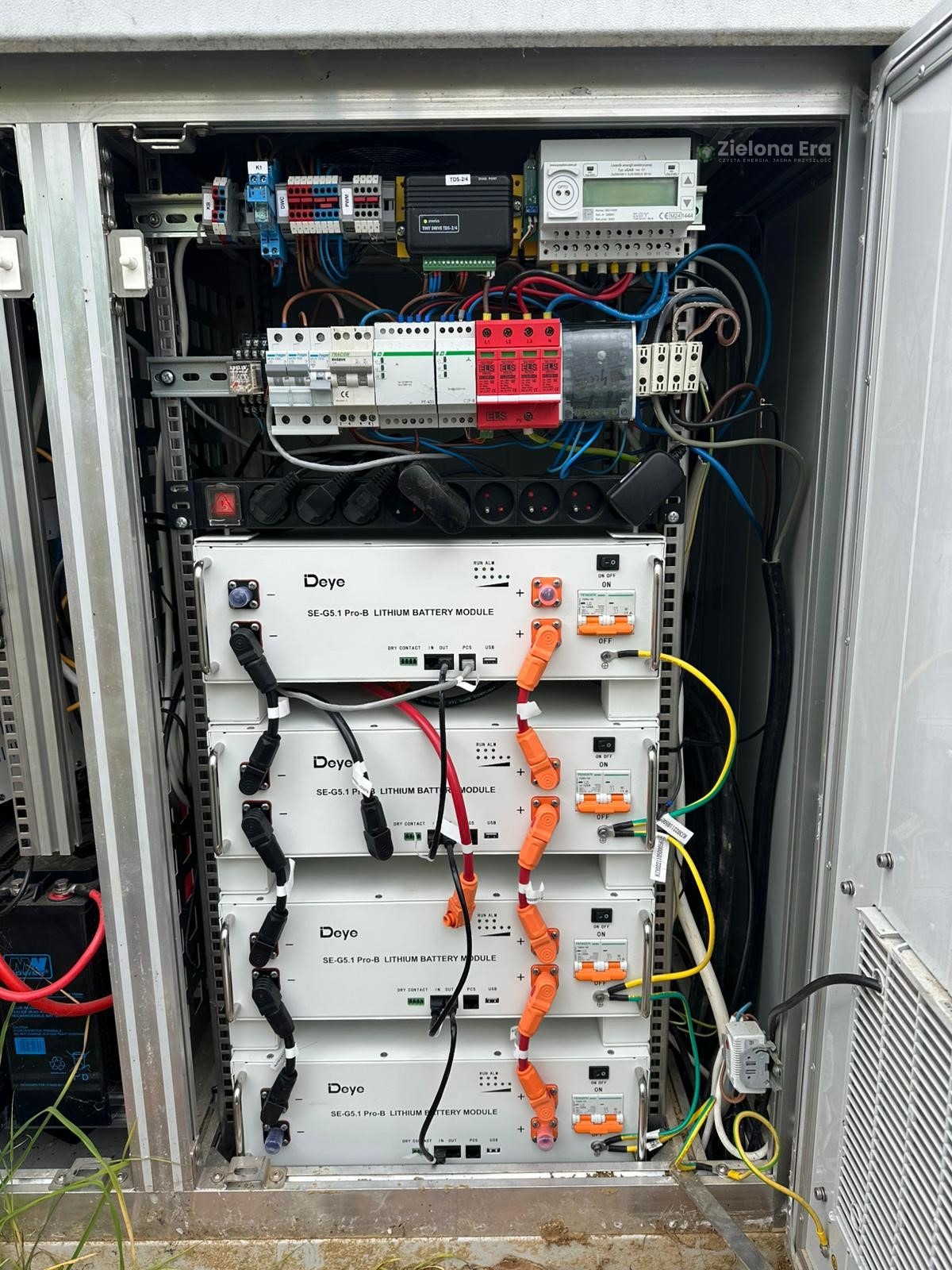 Wnętrze szafy sterowniczej z modułami bateryjnymi Deye SE-G5.1 Pro-B. Widoczne okablowanie, zabezpieczenia i licznik energii. Złożona instalacja wewnątrz metalowej obudowy.