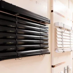 Ekspozycja salonowa: czarne żaluzje z elektrycznym sterowaniem, widoczne inne modele w tle.