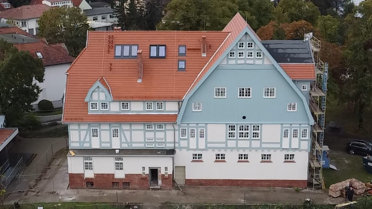 Odnowiona kamienica z czerwonym dachem i błękitną fasadą, widoczne rusztowania z boku budynku.