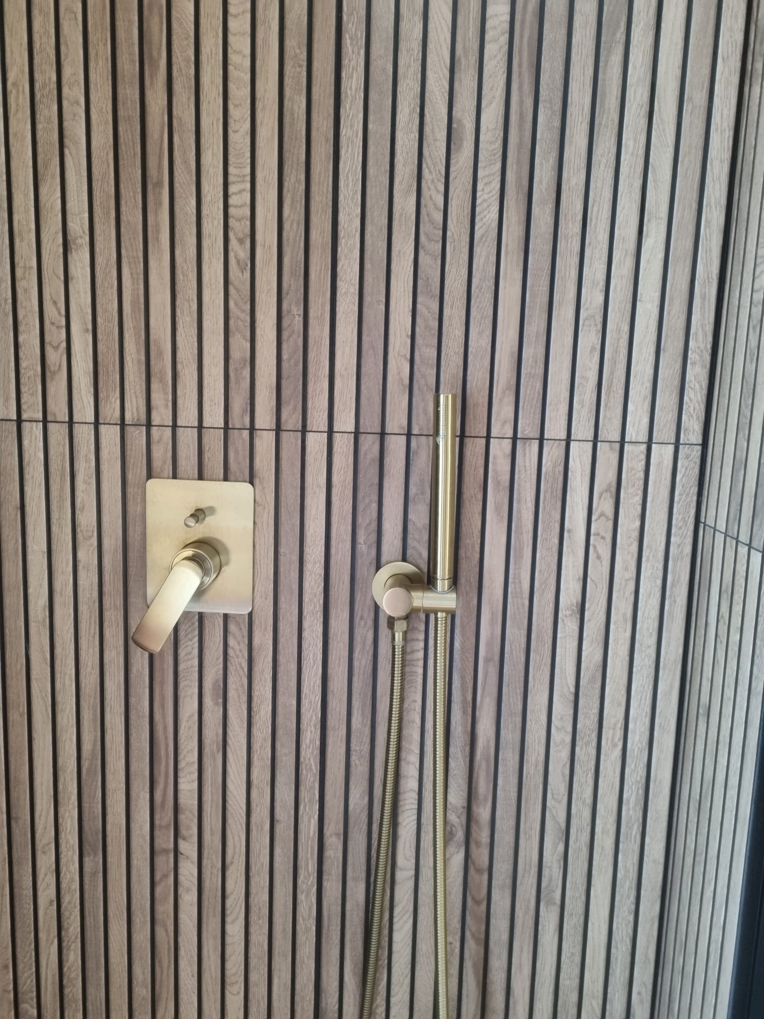 Nowoczesna kabina prysznicowa z drewnianą okładziną ścienną i złotą armaturą. Minimalistyczny design, pionowe panele, eleganckie wykończenie.