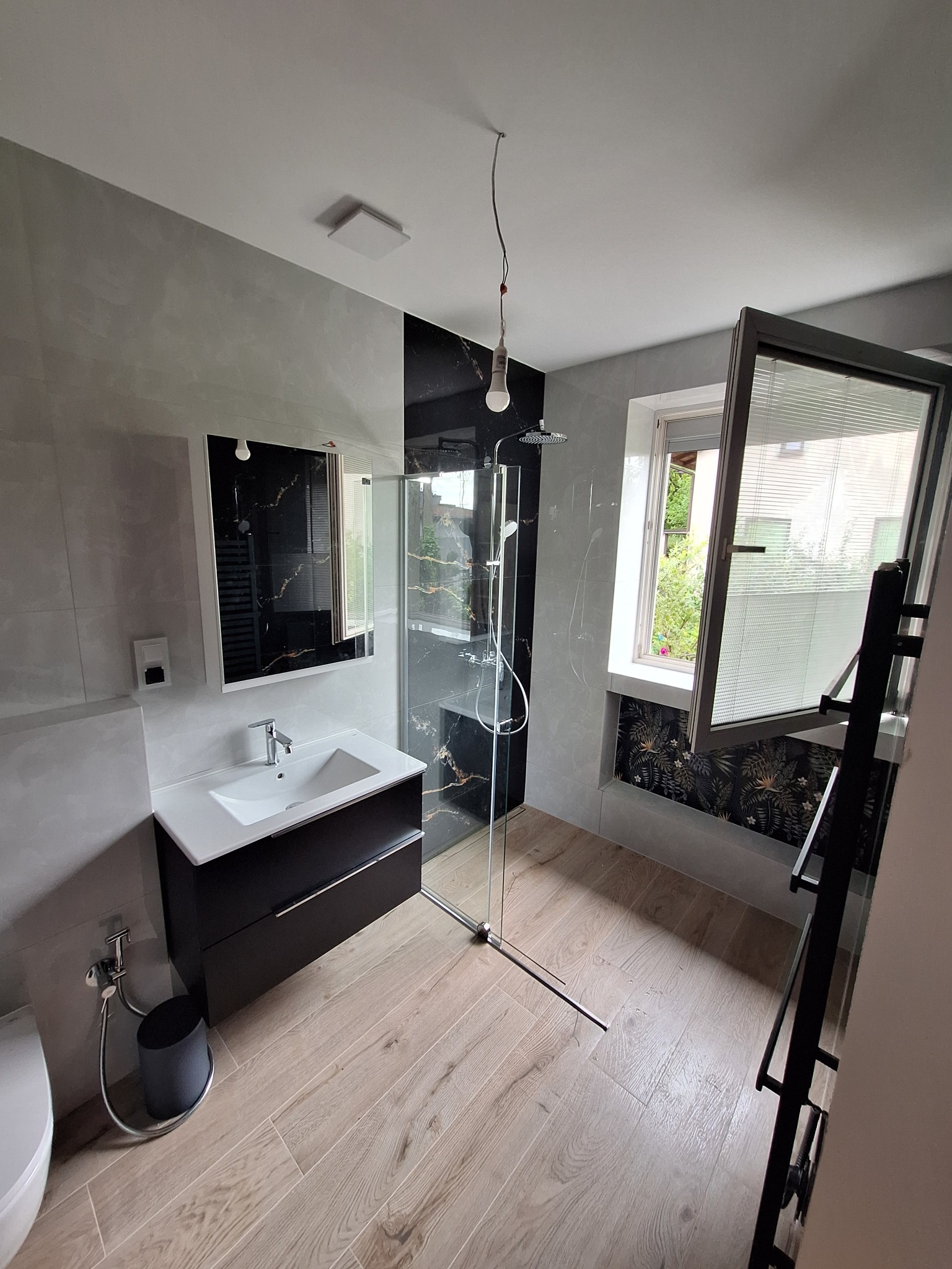 Elegancka łazienka po remoncie: kabina prysznicowa typu walk-in, umywalka z szafką, okno z roletami i egzotyczna tapeta pod parapetem. Nowoczesny design.