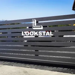 Nowoczesna, pozioma brama przesuwna w kolorze antracytowym z widocznym logo firmy 'LOOKSTAL', częściowo zasłaniająca biały samochód i fragment domu z kamienną elewacją w tle.