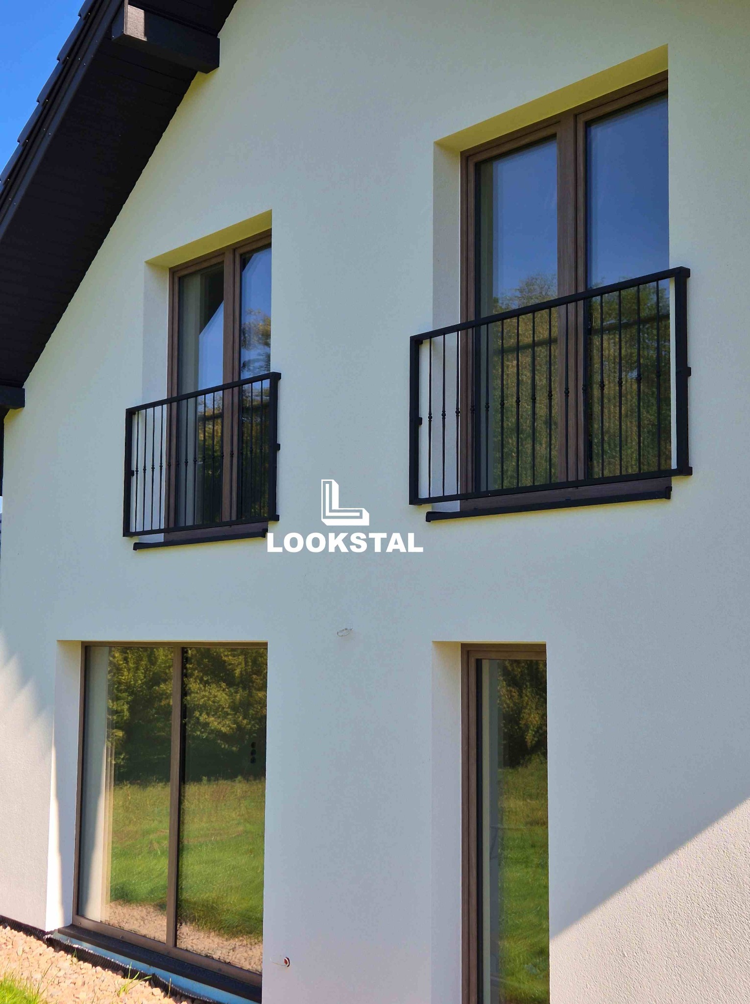 Elewacja domu z oknami balkonowymi zabezpieczonymi czarnymi, metalowymi barierkami. Realizacja z Zakliczyna. Minimalistyczny design, jasna fasada.