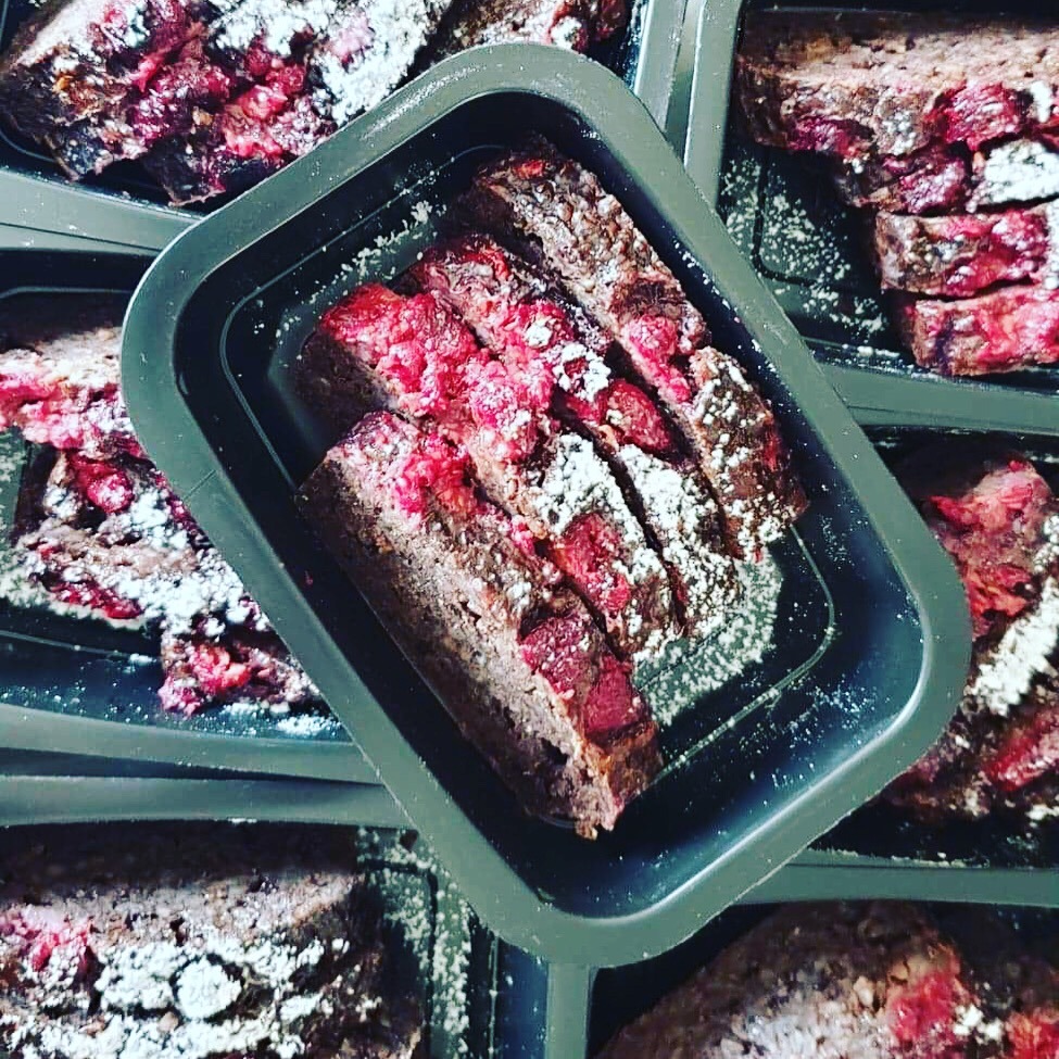 Porcje ciasta czekoladowego z malinami i pudrem w czarnych pojemnikach, ułożone pod kątem, widok z góry.