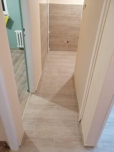 Wykończone wnętrze łazienki w Łodzi z beżowymi płytkami na podłodze i ścianach, widok z korytarza.