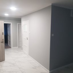 Lulux Krzysztof Cieślicki - Korytarz po odświeżeniu, ściany pomalowane na szaro, białe drzwi z przeszkleniami, podłoga wyłożona białymi płytkami imitującymi marmur.