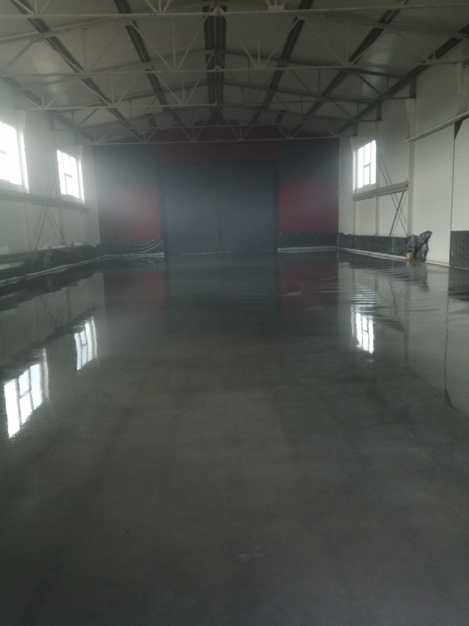 Świeżo wylana, błyszcząca, szara posadzka w hali przemysłowej, z widocznymi oknami i konstrukcją dachu.