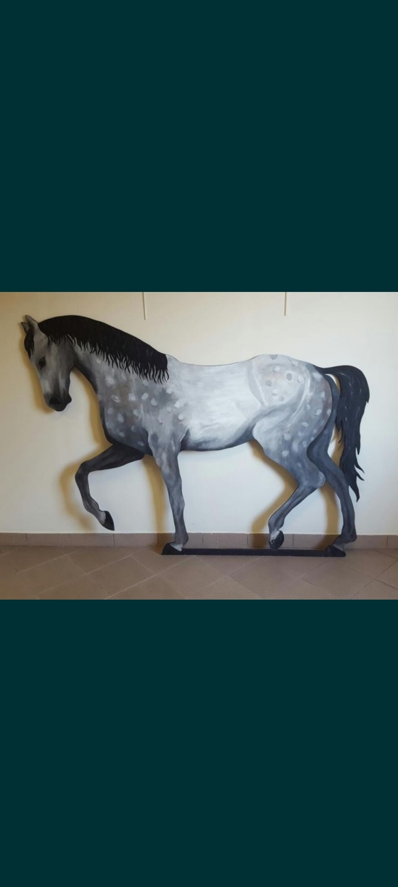 Ręcznie wycinana z płyty MDF, pomalowana na szaro figura konia w naturalnej wielkości, stojąca na podłodze.