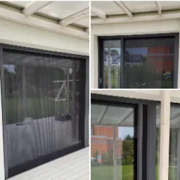 Czarna siatka przeciw owadom zamontowana w ramie okiennej na tarasie, widok na ogród z zewnątrz.