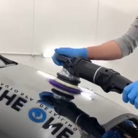 Polerowanie karoserii samochodu za pomocą elektrycznej polerki z nakładką z fioletowej wełny, odbicie logo firmy detailingowej na lakierze.