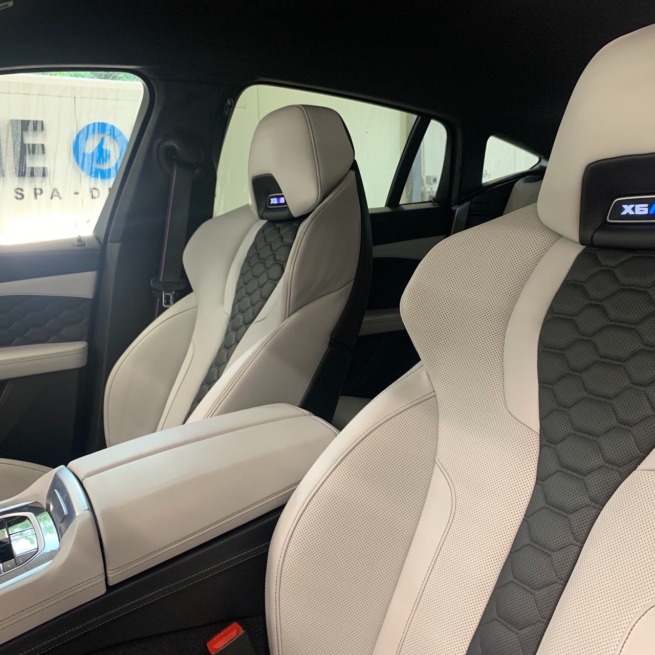 Wnętrze luksusowego samochodu BMW X6 z jasną skórzaną tapicerką, widoczne fotele z perforowanej skóry w kolorze białym i czarnym o strukturze plastra miodu, zagłówki z podświetlanym logo X6, widok...