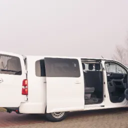 Biały van z otwartymi przesuwnymi drzwiami bocznymi i tylnymi, widoczne wnętrze pojazdu, na zewnątrz mglista pogoda.