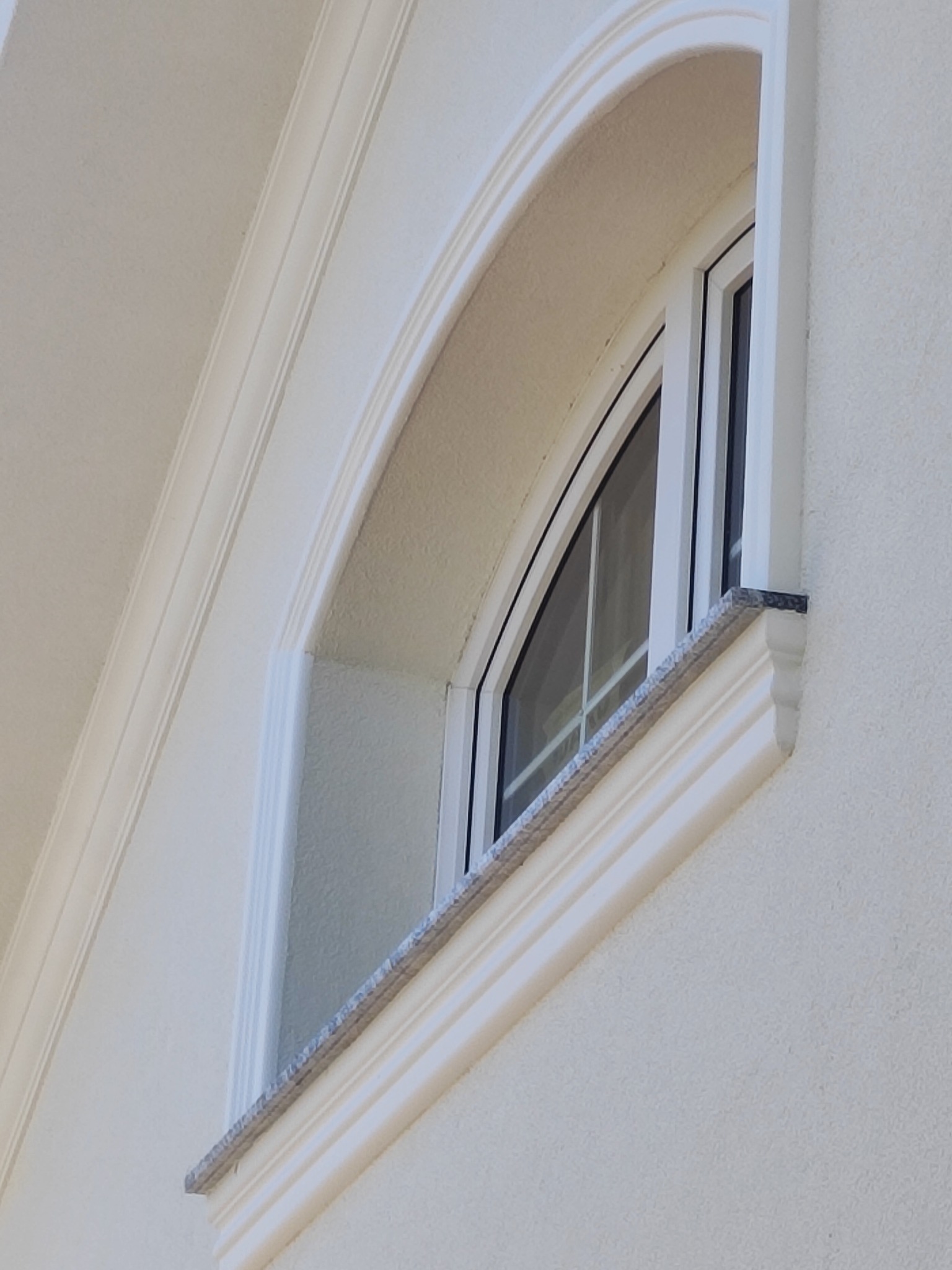 Elewacja budynku z łukowym oknem i dekoracyjnymi listwami. Jasna kolorystyka, widoczne detale wykończenia.