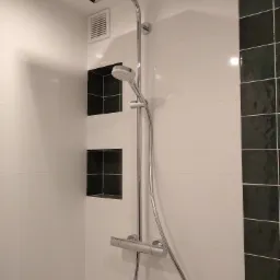 Nowoczesna kabina prysznicowa z chromowaną armaturą, deszczownicą i wnękami wykończonymi ciemną glazurą na białych płytkach ściennych.