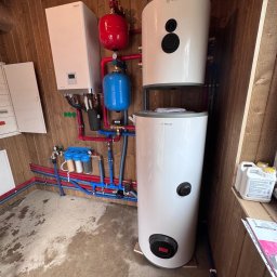 ELTROCOM SP. Z O.O. - Kotłownia z dwoma zbiornikami Rotenso, bojlerem, filtrami wody i rozbudowaną instalacją hydrauliczną w pomieszczeniu wykończonym boazerią.