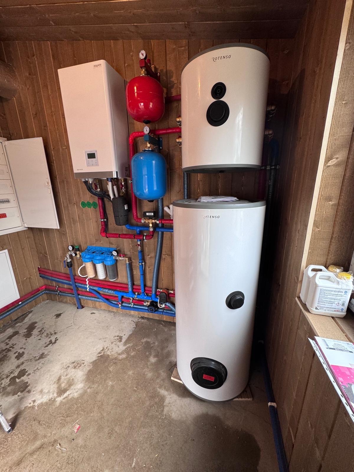 Kotłownia z dwoma zbiornikami Rotenso, bojlerem, filtrami wody i rozbudowaną instalacją hydrauliczną w pomieszczeniu wykończonym boazerią.