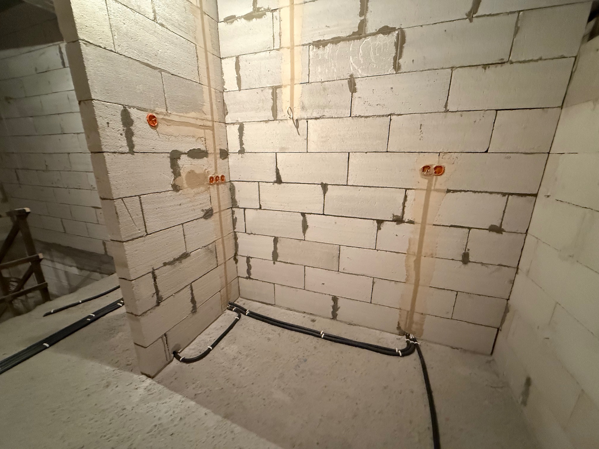 Surowy stan: białe bloczki, instalacja elektryczna w bruzdach i podłodze, pomarańczowe puszki. W tle widoczny fragment drabiny.