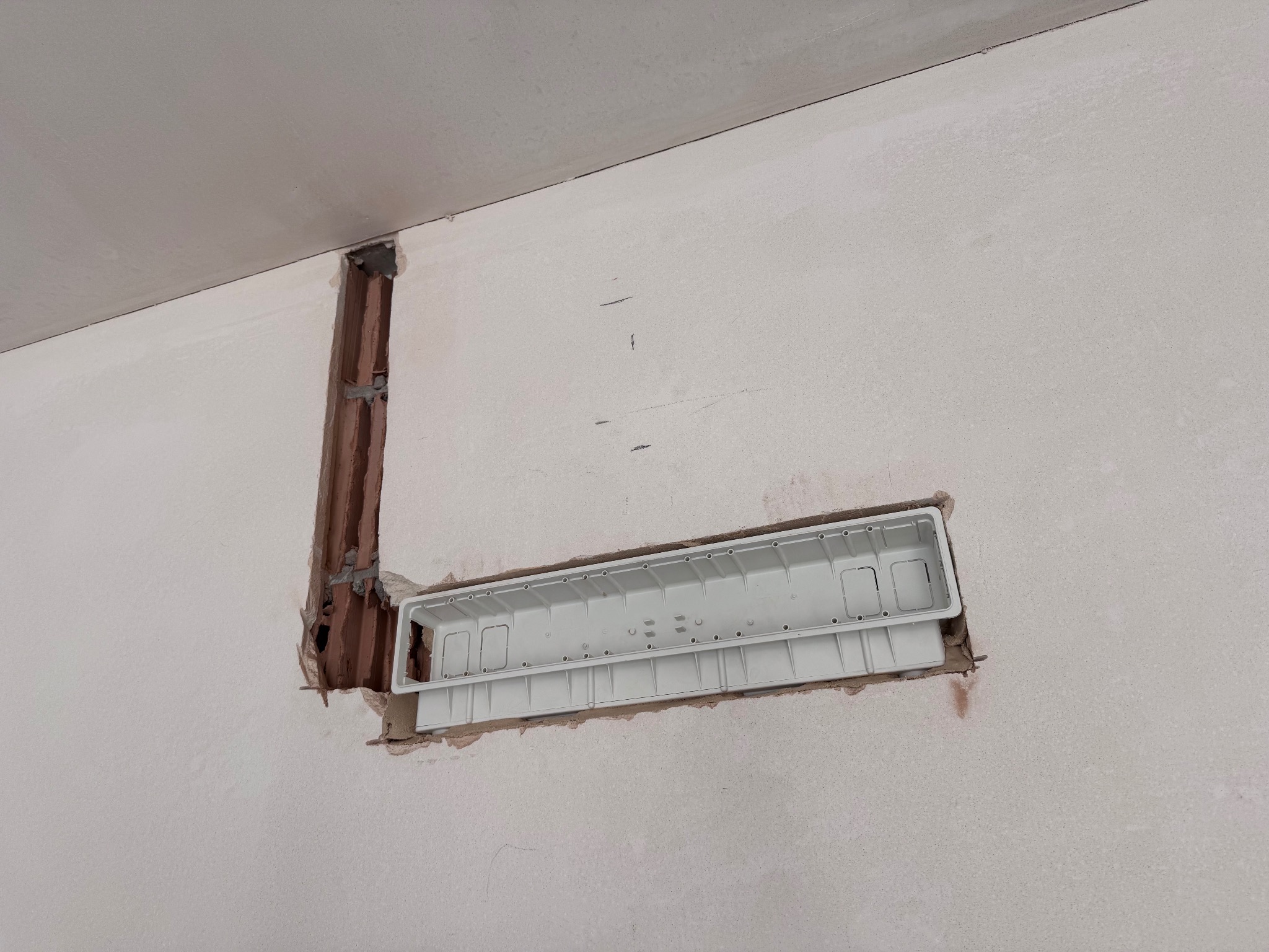 Wnęka w ścianie z zamontowaną białą puszką podtynkową, widoczne ślady po kuciu i pionowa bruzda. Przygotowanie do instalacji elektrycznej.