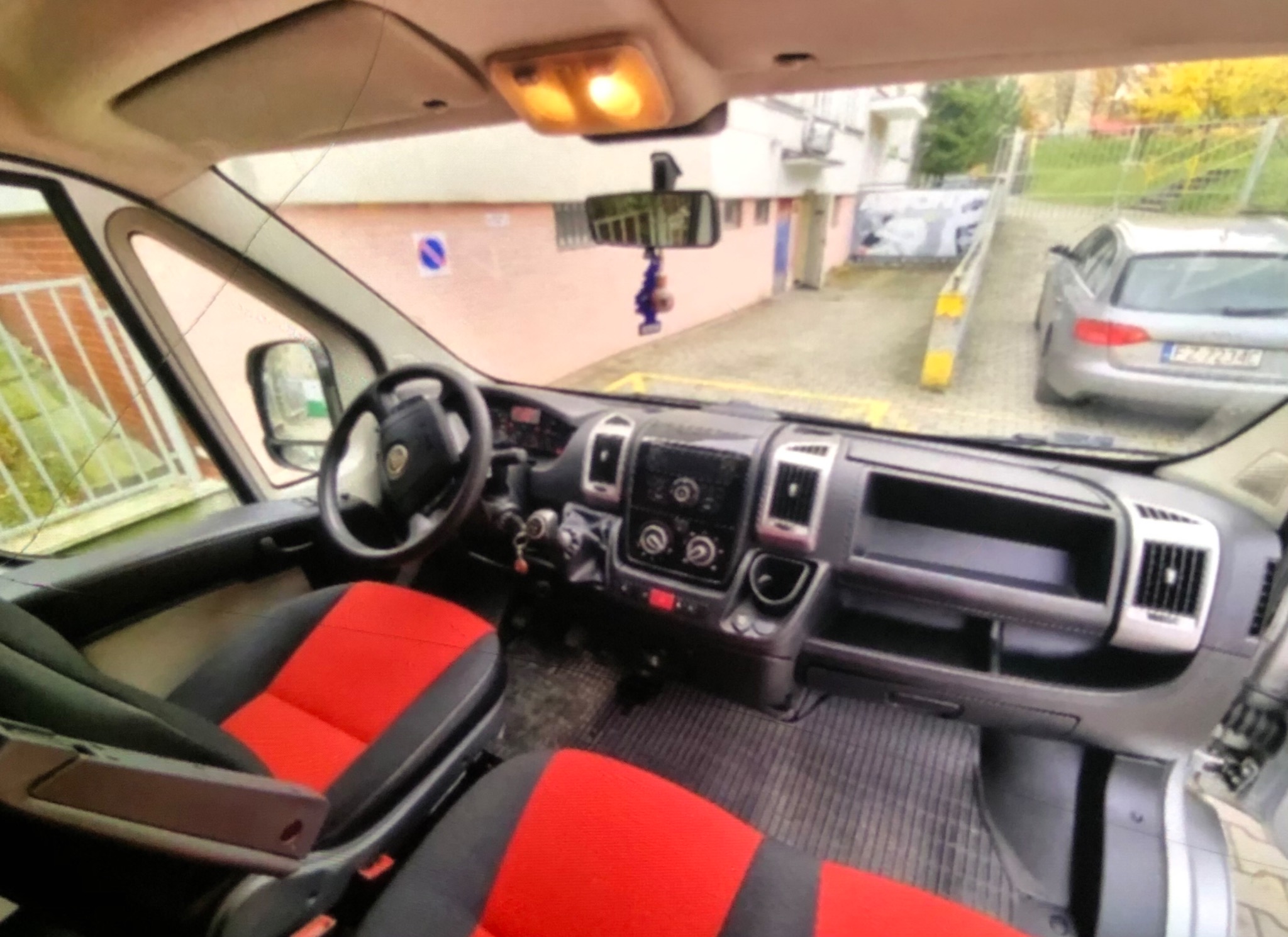 Wnętrze busa z czerwono-czarnymi pokrowcami na siedzeniach, widok z perspektywy kierowcy na deskę rozdzielczą i ulicę.