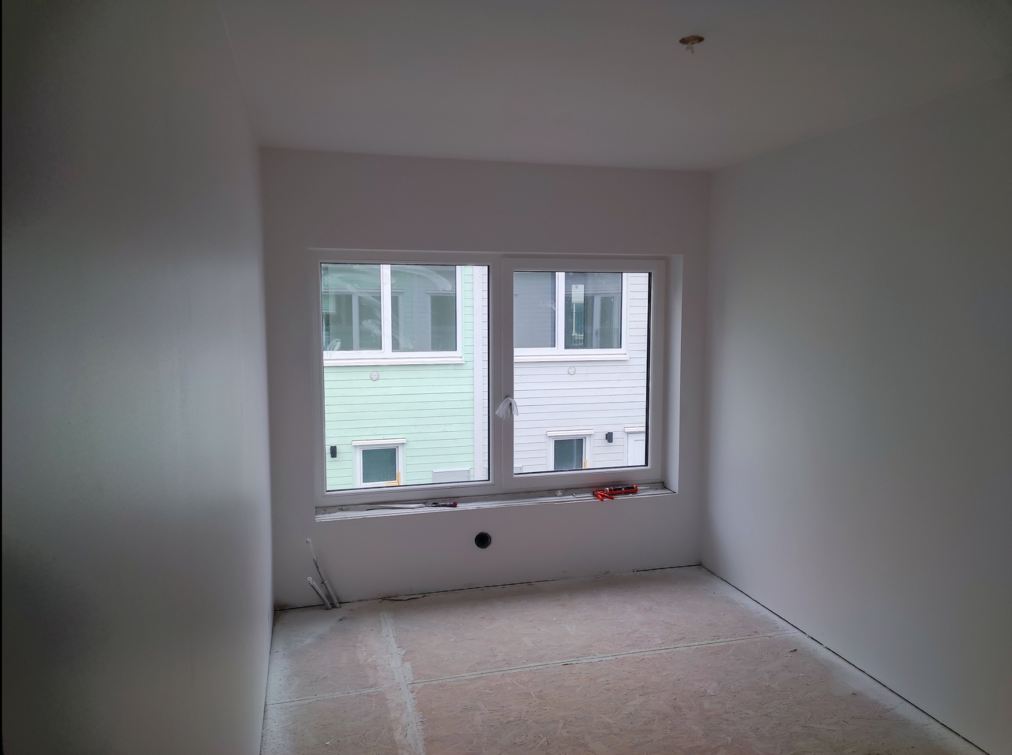 Wnętrze pokoju w trakcie wykańczania, ściany i sufit świeżo wyszpachlowane na gładko, widoczne narzędzia na parapecie okna, podłoga przygotowana pod dalsze prace.