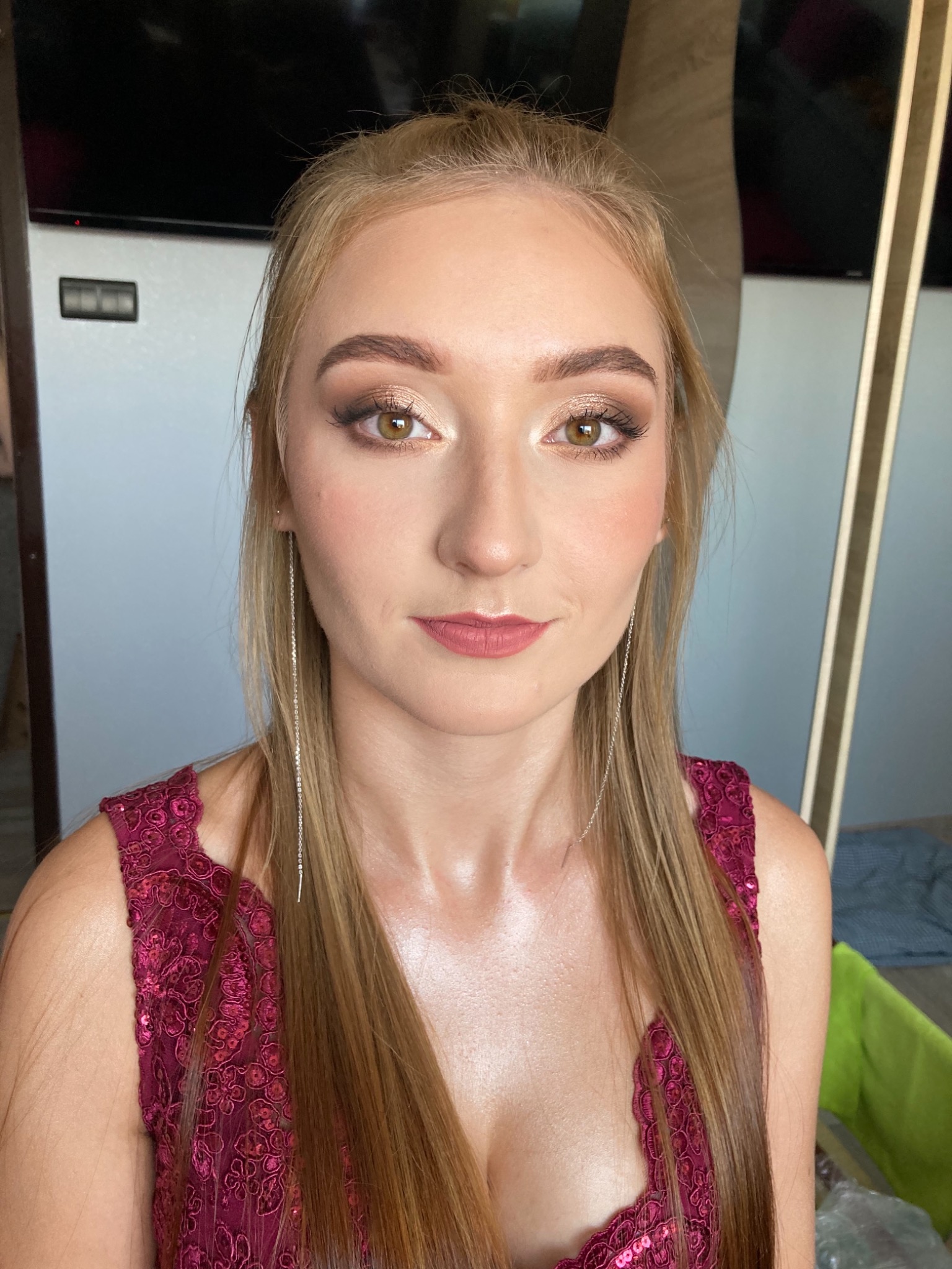 Portret kobiety z profesjonalnym makijażem oczu w odcieniach złota i brązu, podkreślonymi brwiami i delikatnymi ustami w kolorze różu, uzupełniony długimi, srebrnymi kolczykami łańcuszkowymi...