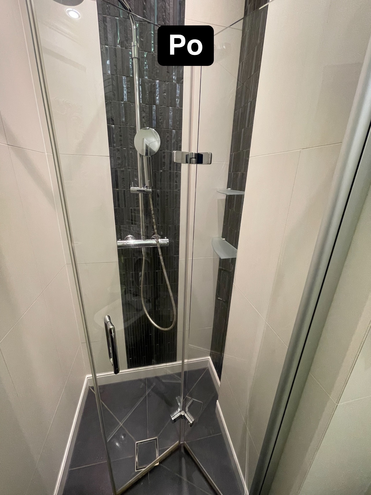 Nowoczesna kabina prysznicowa z czarno-białymi płytkami, widok z góry na chromowany zestaw natryskowy i czarny odpływ w podłodze.