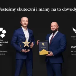 Dwóch mężczyzn w garniturach prezentuje nagrody dla WGN Sosnowiec: 'Lider Nieruchomości 2021' oraz 'Orzeł Broker WGN 2020', potwierdzające skuteczność w branży.