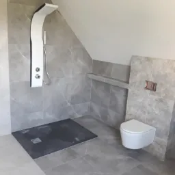 Nowoczesna łazienka w Sidzinie na poddaszu, wykończona szarymi płytkami imitującymi marmur, z kabiną prysznicową z panelem natryskowym i podwieszaną toaletą.