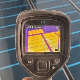 Samurio sp. z o.o. - Pomiar temperatury termowizyjnej zainstalowanej podłogowej instalacji grzewczej, widoczne rury grzewcze pod podłogą na ekranie kamery termowizyjnej, w tle fragment pomieszczenia z białą ścianą.