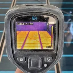 Samurio sp. z o.o. - Pomiar temperatury rozłożonej maty grzewczej za pomocą kamery termowizyjnej, widoczny ekran urządzenia z nałożonym obrazem termicznym.